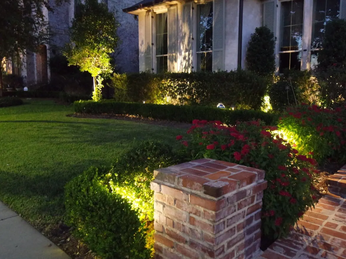 Front yard landscape lighting with uplighting on shrubs, trees, and flower beds near a brick entryway