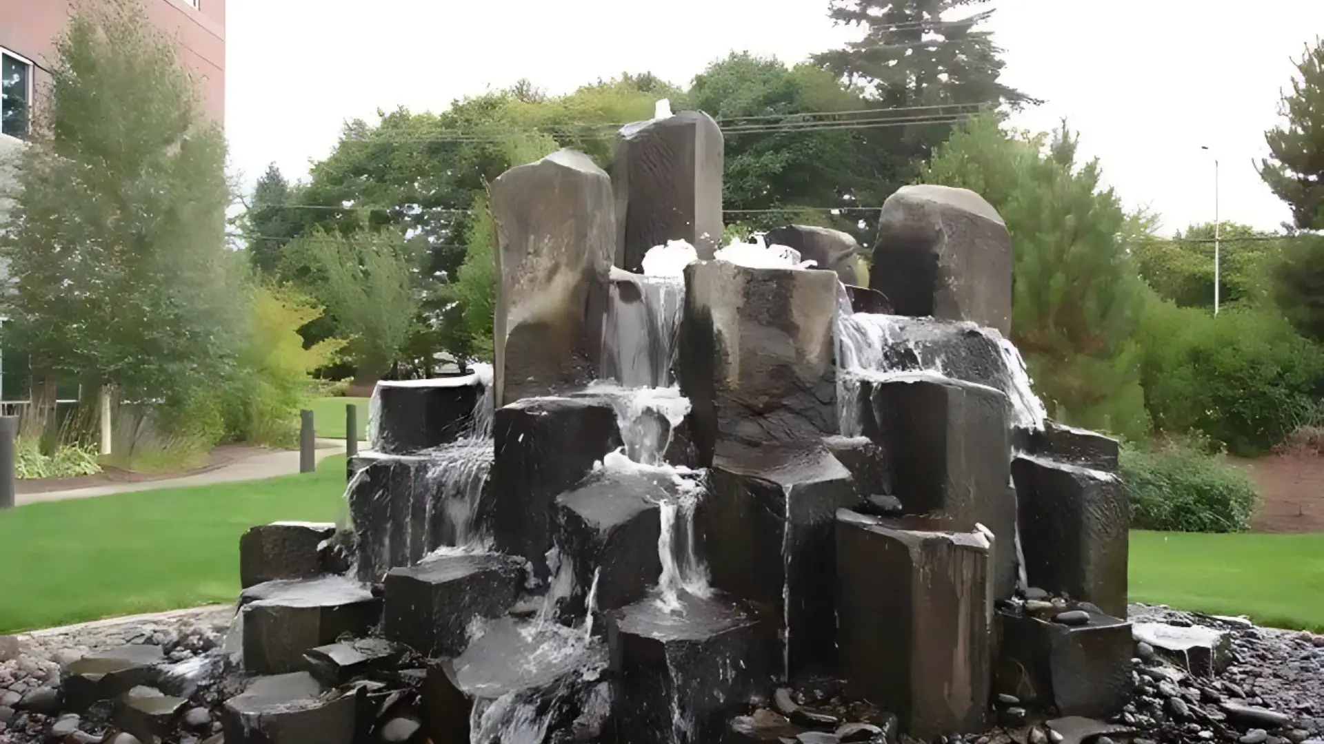 Modern stone water feature with cascading water flowing over natural basalt columns surrounded by decorative river rock
